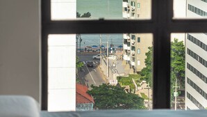 Une chambre avec vue sur l’océan, accessible par une fenêtre, comprenant un lit et offrant un panorama sur la ville, avec ses bâtiments et ses rues.