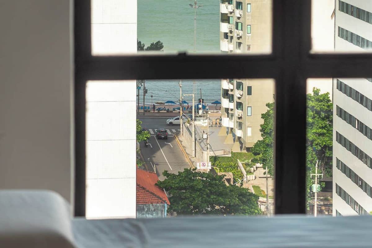 Habitación con vista al océano a través de una ventana, que incluye una cama y una vista del paisaje urbano con edificios y una calle.