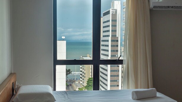 Une chambre d’hôtel avec un lit, une fenêtre donnant sur la mer et des bâtiments.