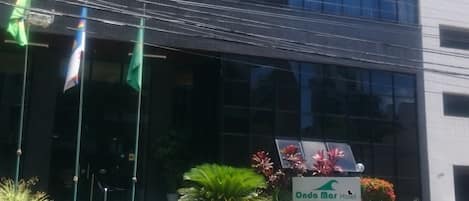 Un edificio moderno con fachada de vidrio, un cartel del Hotel Onda Mar y varias banderas al frente.