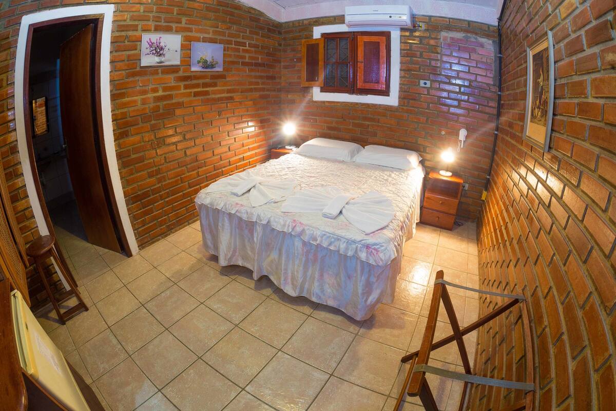 A bedroom with a brick wall, a bed with a white bedspread, a nightstand, and a wooden ladder.