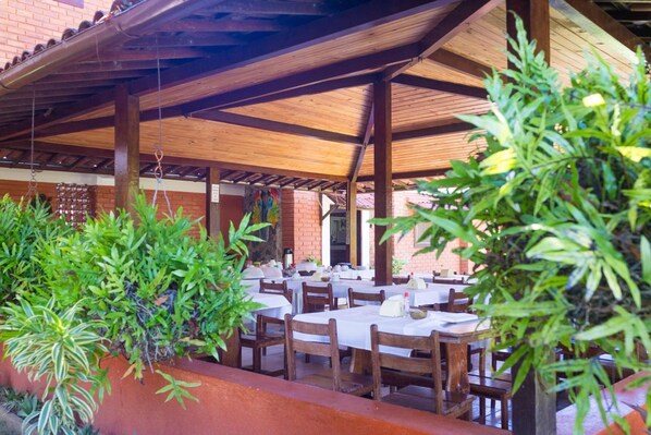 An outdoor patio with tables and chairs, surrounded by greenery and brick walls. - Real Pousada (Ipojuca)