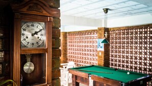 Una mesa de billar y un reloj en una habitación con pared de ladrillo y un papel tapiz decorativo al fondo.