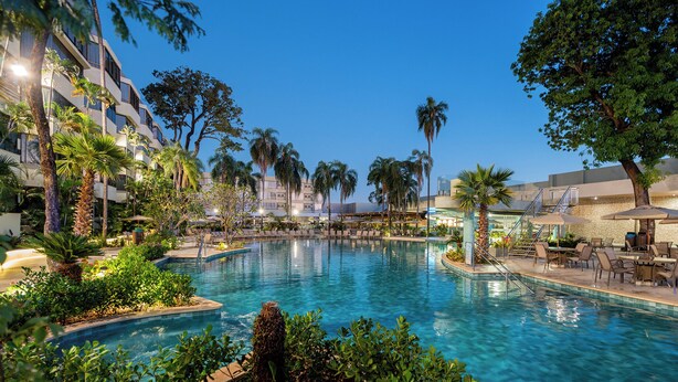 Una piscina rodeada de palmeras y sillas de descanso, con un edificio al fondo.