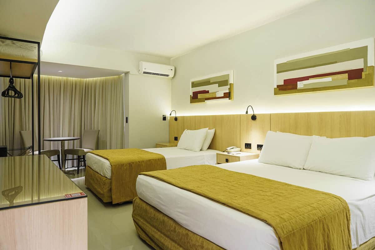 A hotel room with two beds, a desk, a chair, a mirror, and an air conditioning unit.