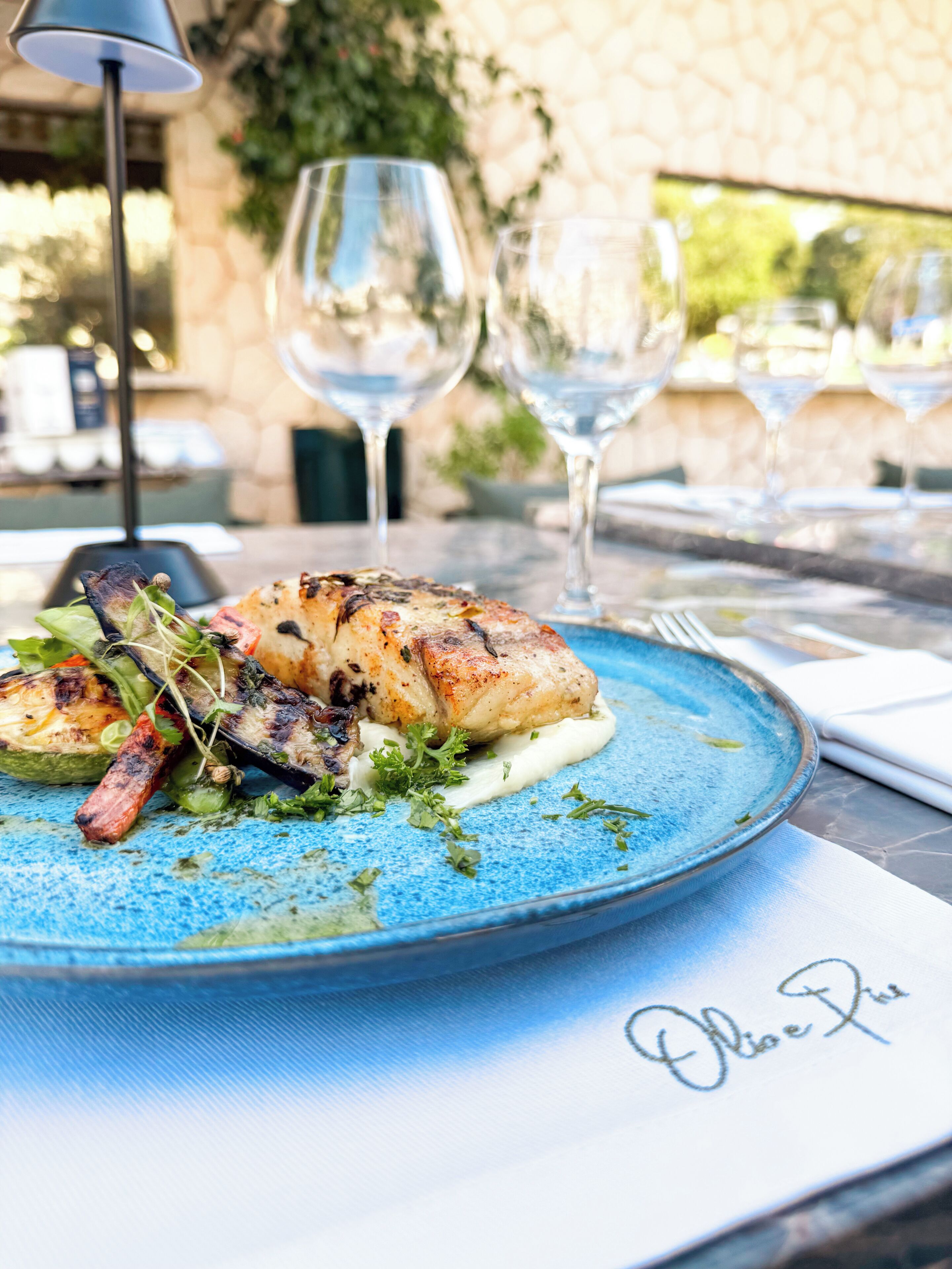 A plate of food with grilled meat and vegetables, accompanied by wine glasses on a table.