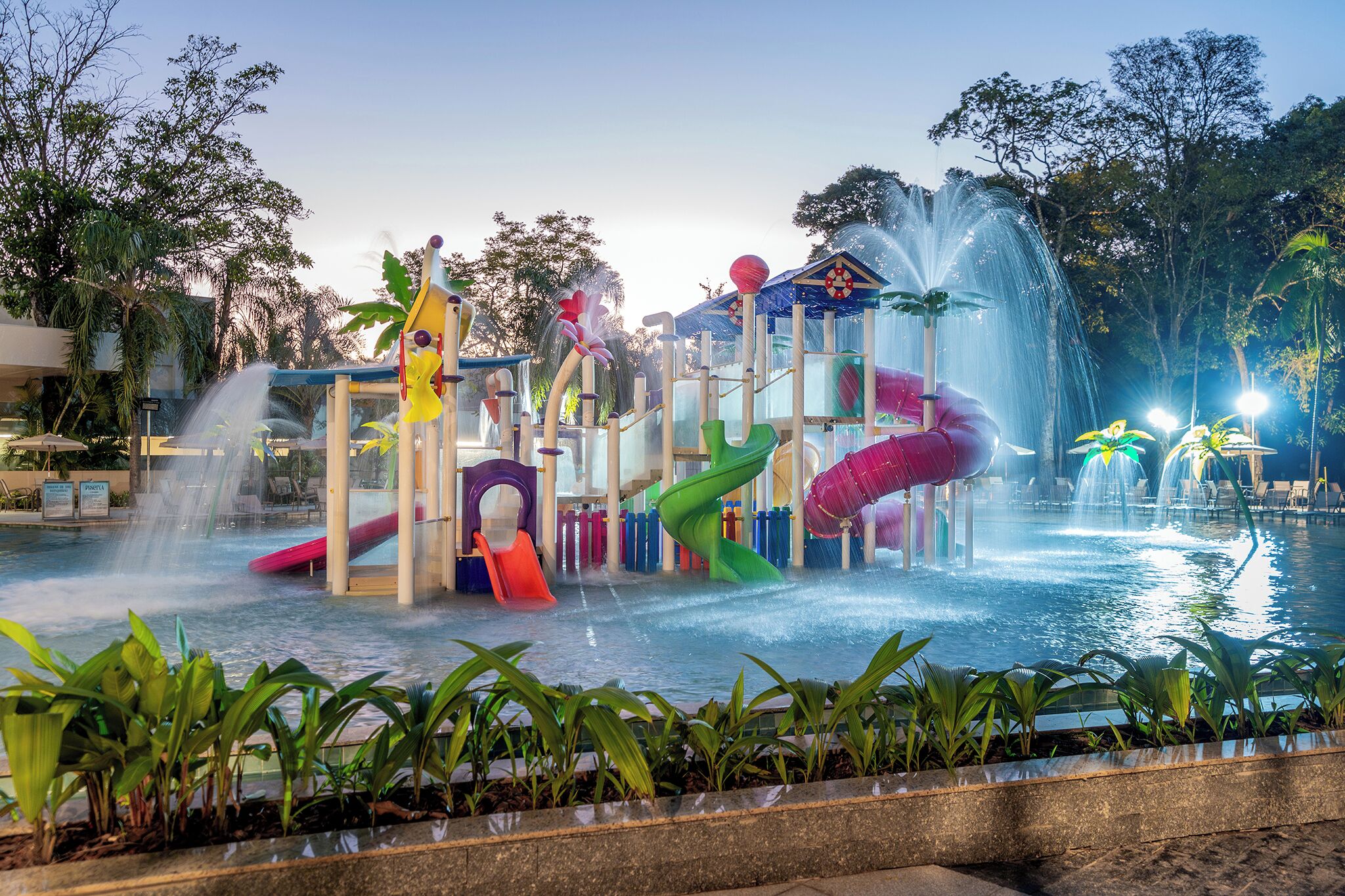 Area giochi con acqua, scivoli e fontane, immersa nel verde.