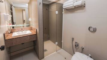 A modern bathroom with a granite countertop sink, a glass shower enclosure, and a toilet with a towel rack above it.