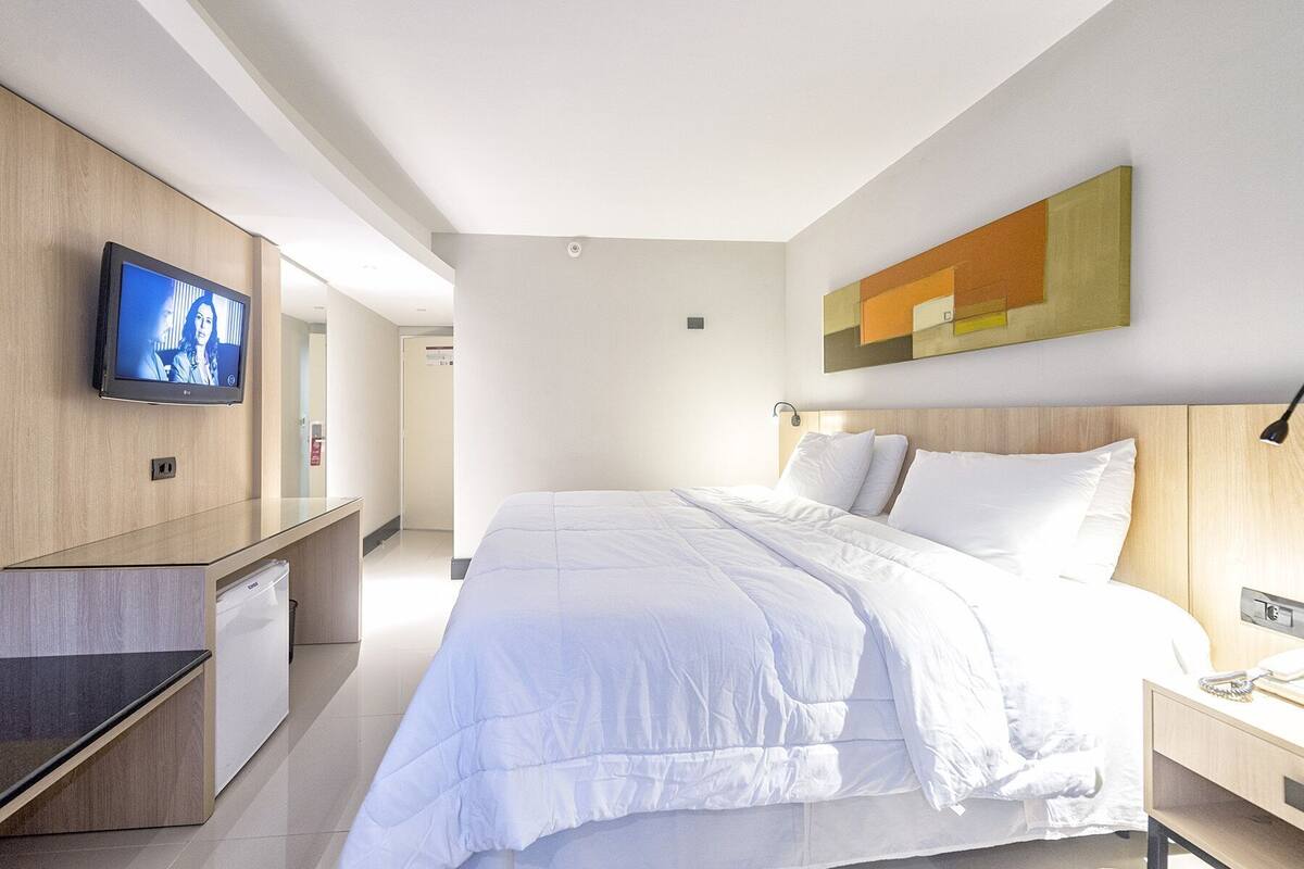 A modern hotel room with a bed, a TV mounted on the wall, a desk, and a painting.