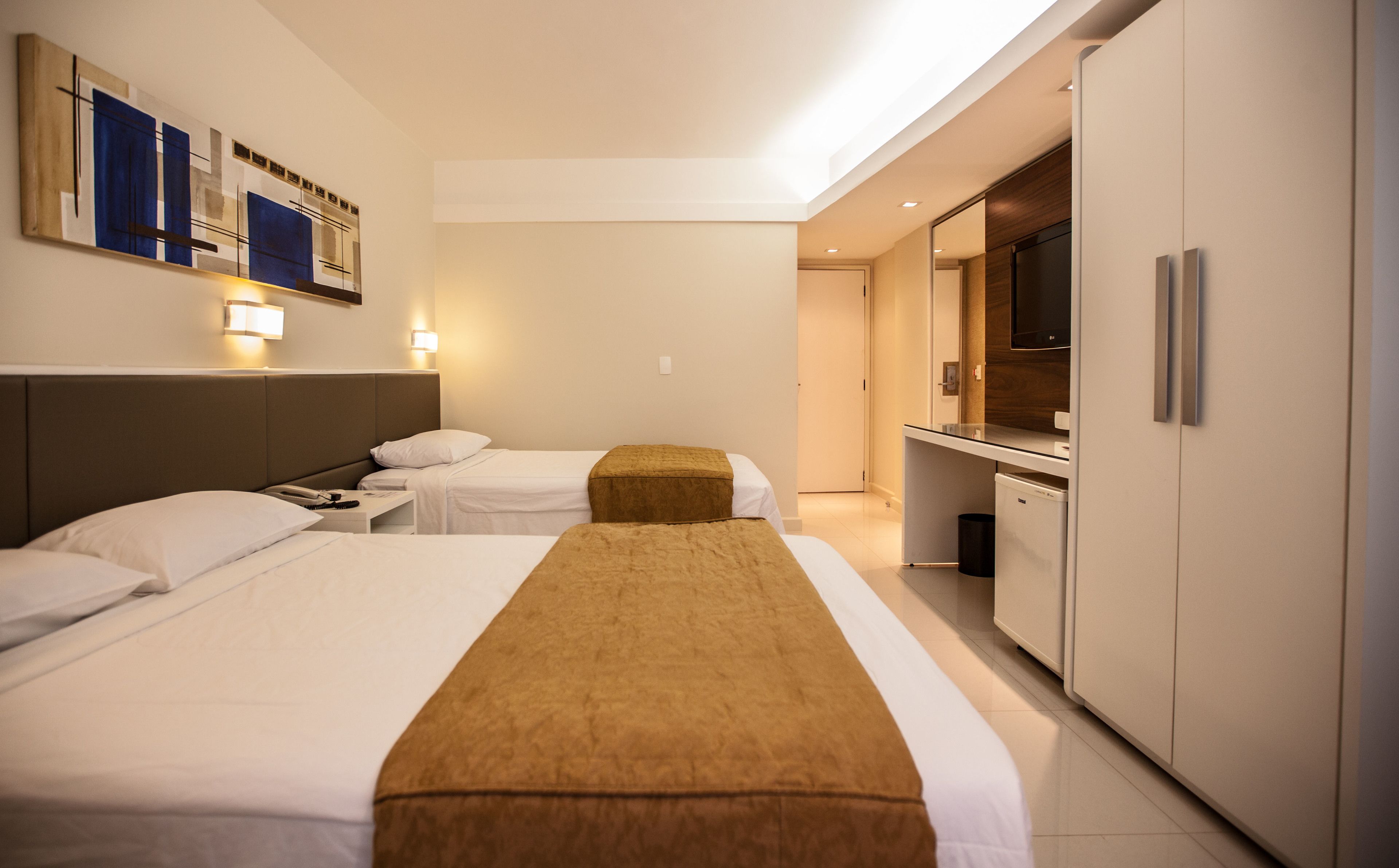 A hotel room with two beds, a minibar, a television, and a wall-mounted artwork.