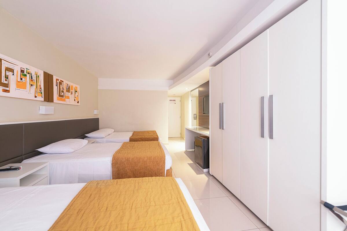 A hotel room with two beds, a wardrobe, a desk, and a television.