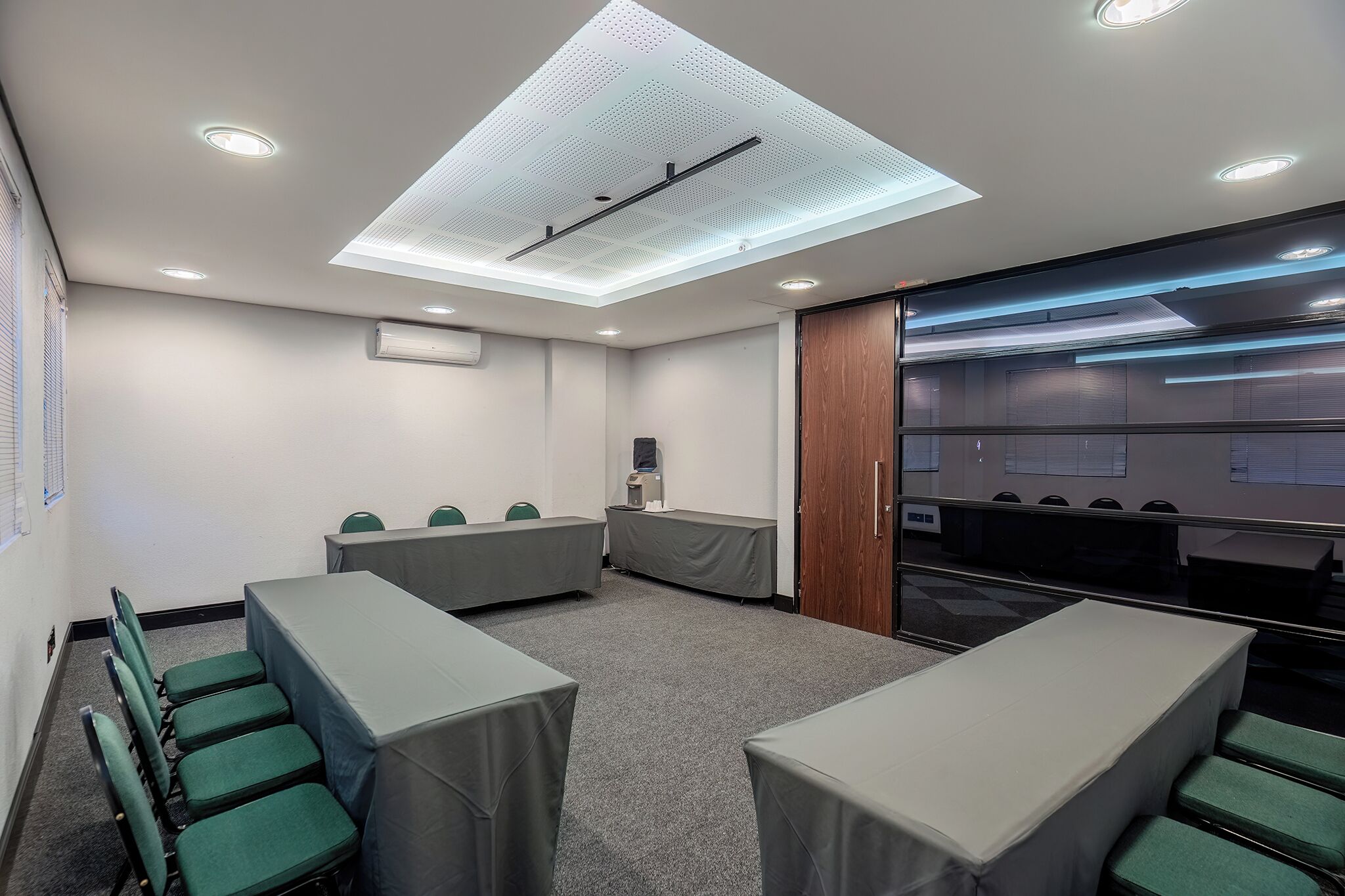 Un salón de conferencias con techo alto, iluminación empotrada y un ventanal grande.