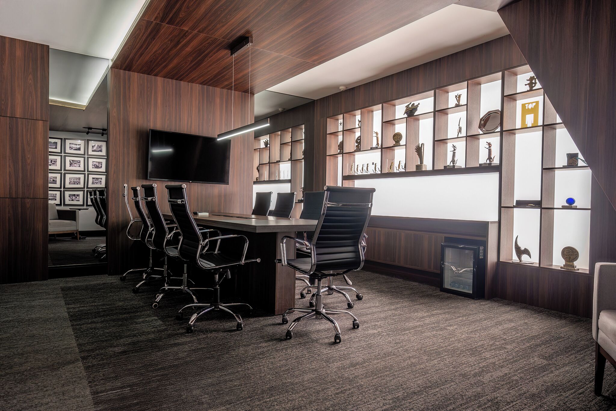 A modern conference room with a long table, multiple chairs, a large flat-screen TV, and a wall of shelves with decorative items.