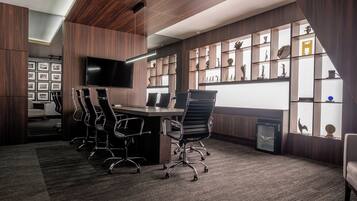 A modern conference room with a long table, multiple chairs, a large flat-screen TV, and a wall of shelves with decorative items.
