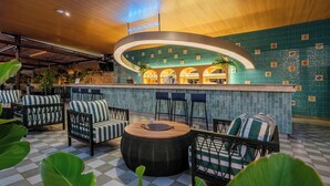 Una zona de bar con barra curva, mobiliario de mimbre y suelo a cuadros.
