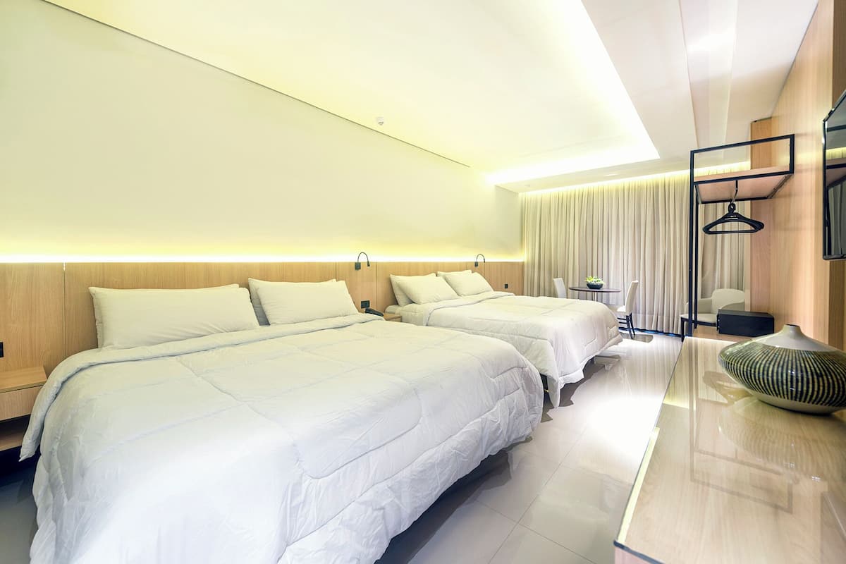 A hotel room with two beds, a bedside table, a small table with a plant, and a hanging light fixture.