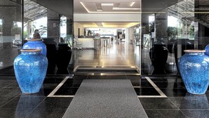 Un moderno vestíbulo de hotel con entrada de vidrio, dos grandes jarrones azules, un mostrador de recepción y un piso de baldosas limpias.