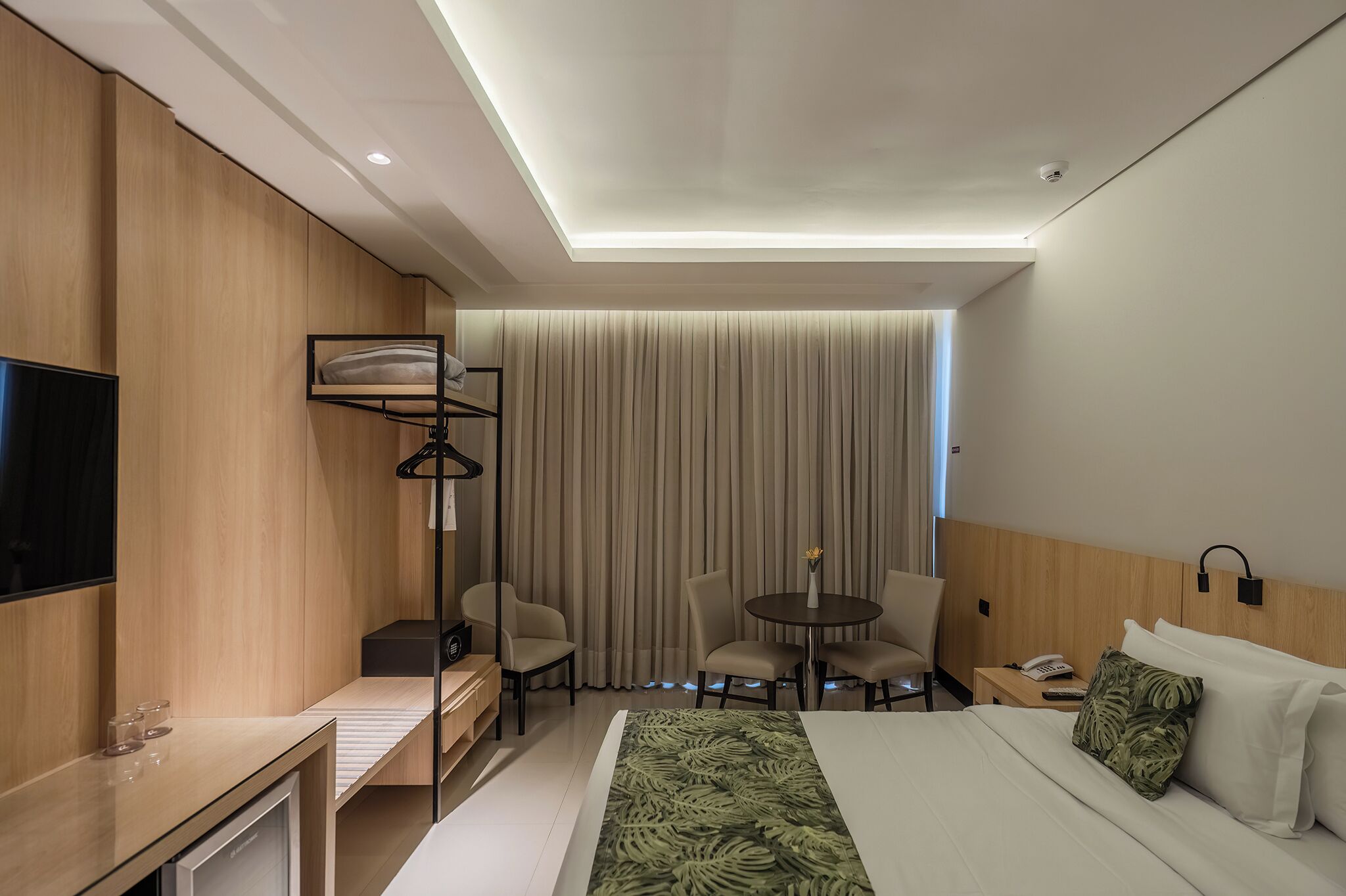 A hotel room with a bed, bedside table, desk, chair, and a TV.