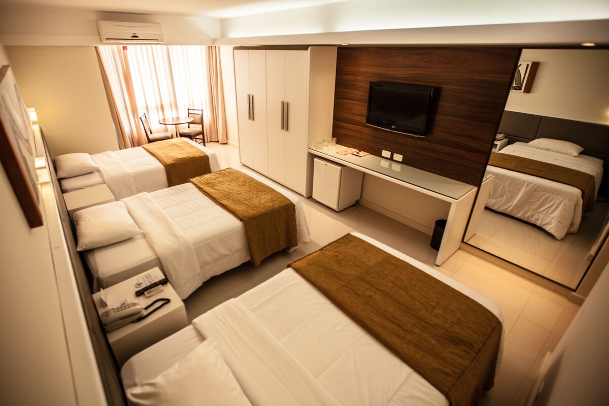 A hotel room with two beds, a desk, a TV, and a mirror.
