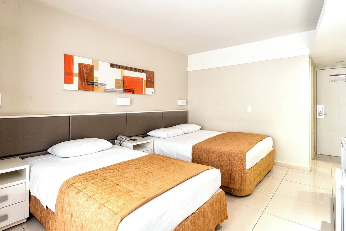 A hotel room with two beds, a nightstand, a desk, and a mirror.