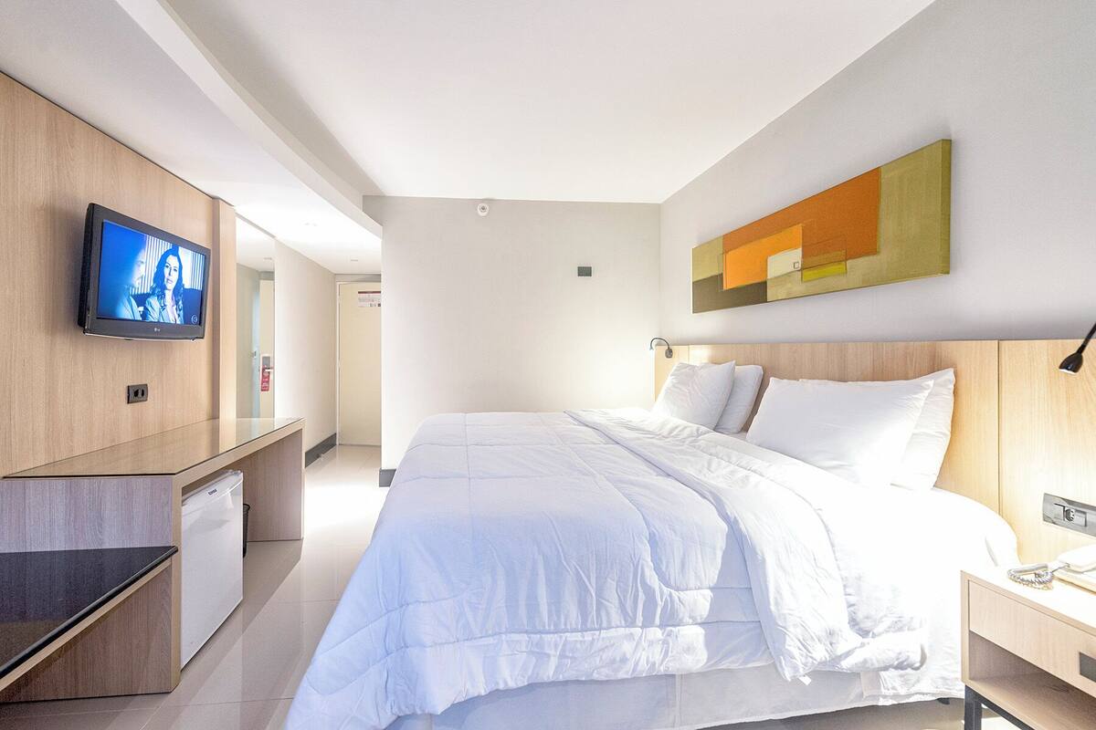A modern hotel room with a large bed, a TV mounted on the wall, and a minimalist design.