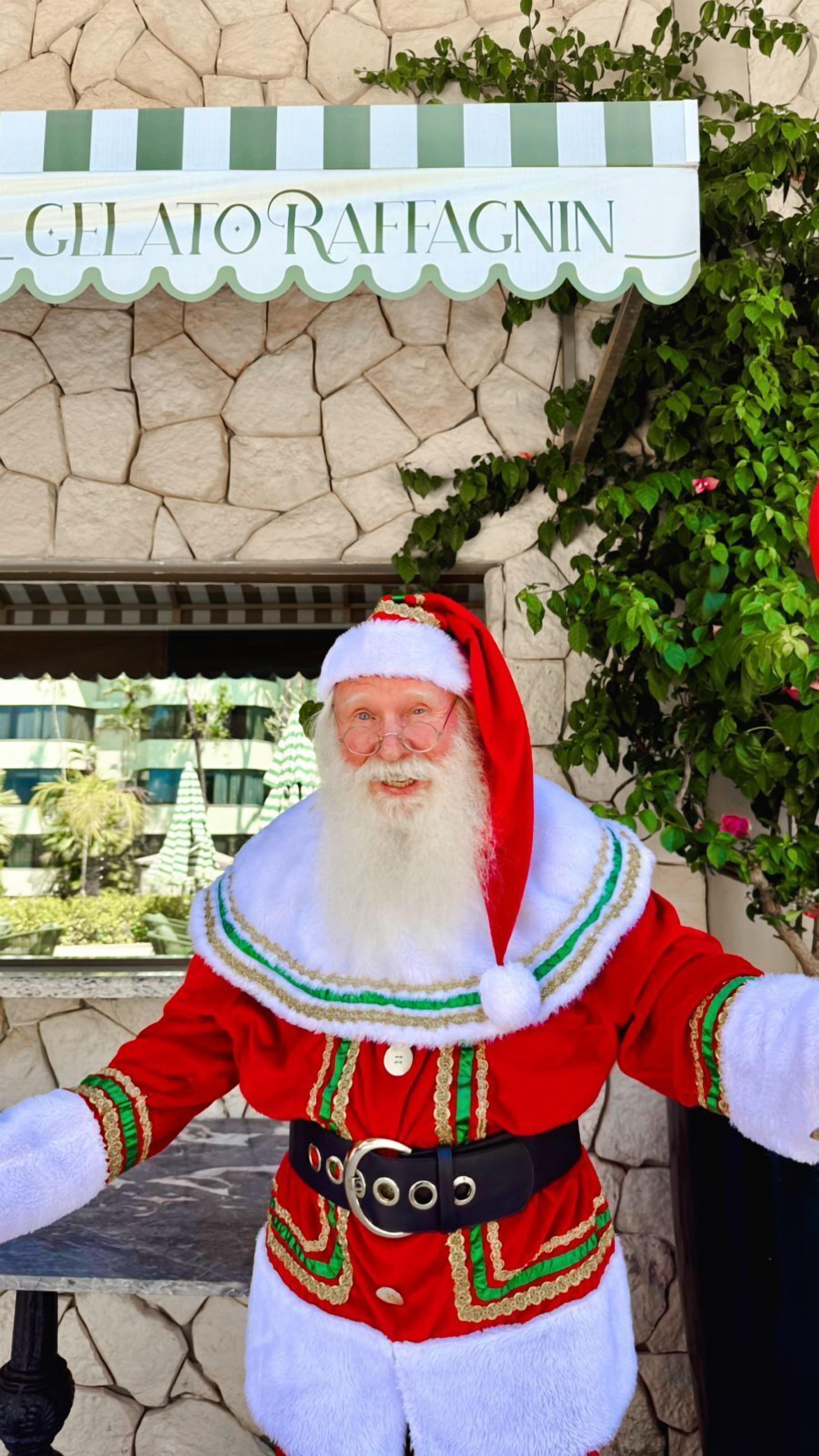 A person in a Santa Claus costume standing in front of a sign that reads "GELATO RAFFAGNIN".