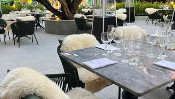 Een buiten eethoek met marmeren tafels, zwarte rieten stoelen met witte bontponpon en een centrale boom.