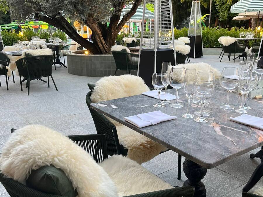 Een buiten eethoek met marmeren tafels, zwarte rieten stoelen met witte bontponpon en een centrale boom.