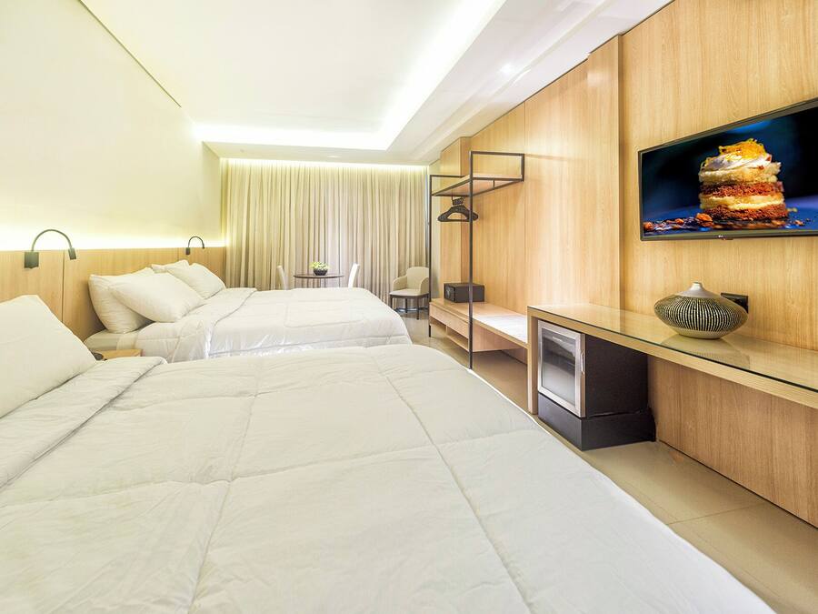 A hotel room with two beds, a desk, a television, and a small table with a plant.