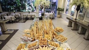 Un bufé con diversas opciones de panadería y pastelería, dispuesto en una mesa amplia en una habitación bien iluminada y con vistas al exterior.
