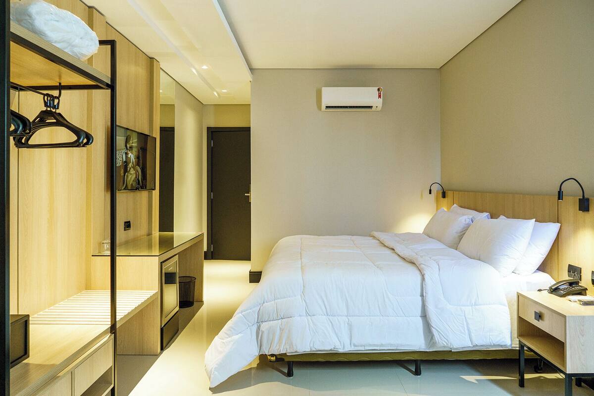 A hotel room with a bed, bedside table, lamp, and a wardrobe with a mirror.