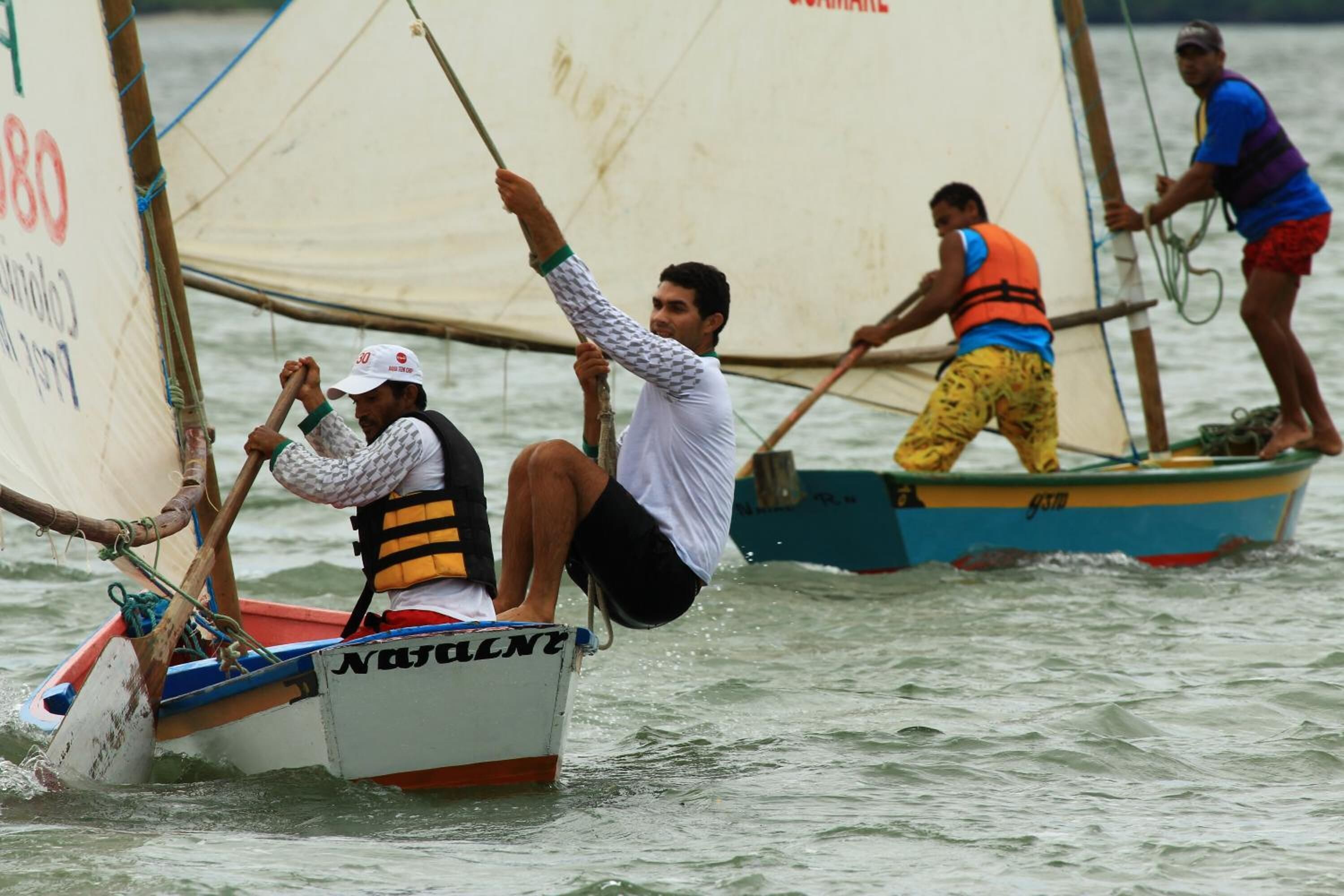 A group of people on a sailboat with a white hull and blue accents, engaged in sailing activities.
