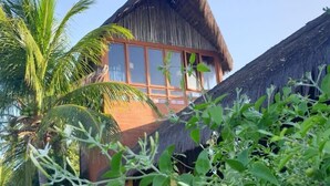 Un edificio con techo de paja y ventanas amplias, rodeado de exuberante vegetación y una terraza de madera.