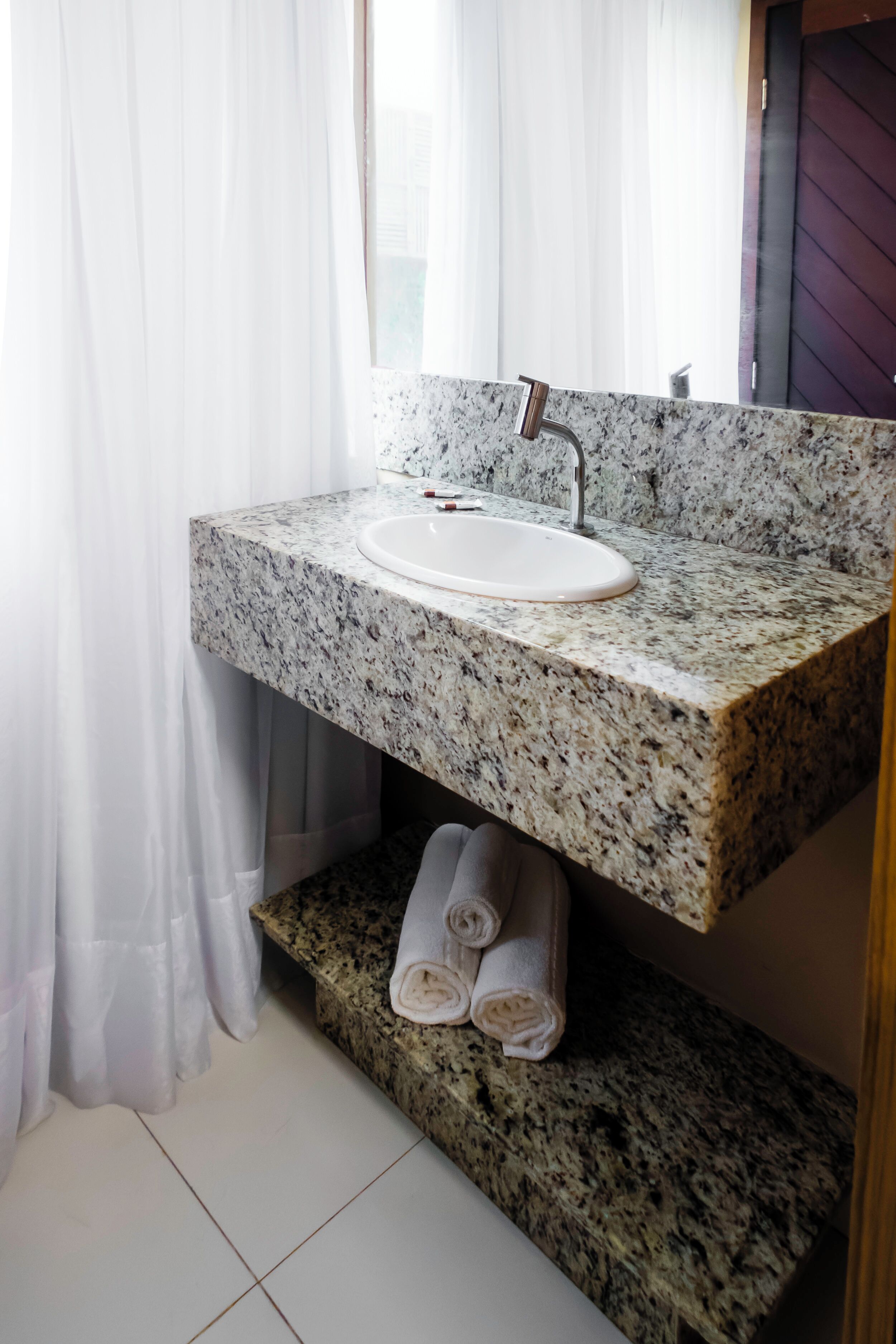 Un baño con lavamanos de encimera de granito, un espejo encima y un perchero con toallas.