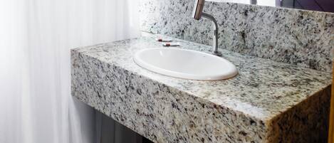 Un baño con lavamanos de encimera de granito, un espejo encima y un perchero con toallas.