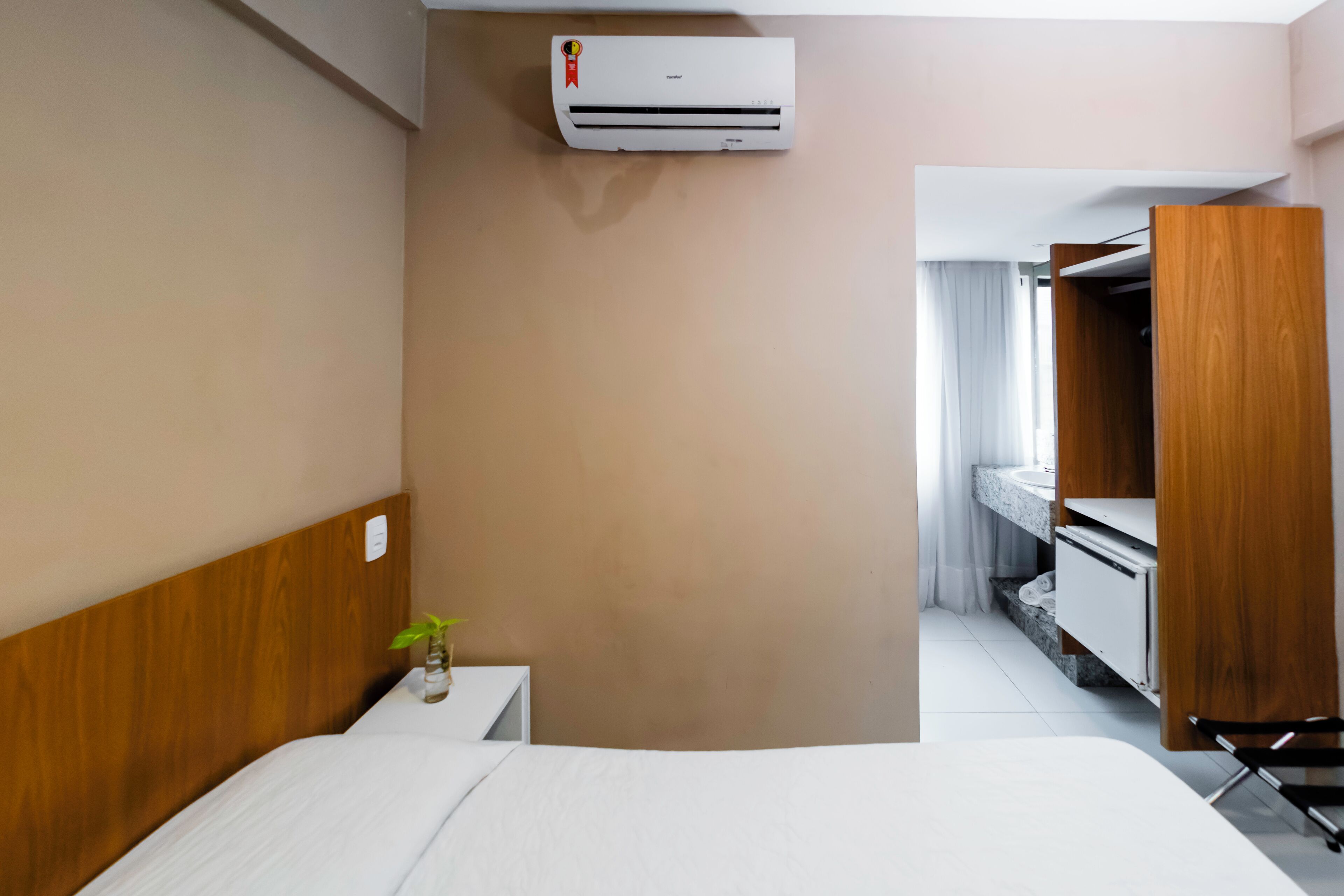 Een hotelkamer met een bed, een klein nachtkastje met een plant, een kledingkast en een airconditioning.