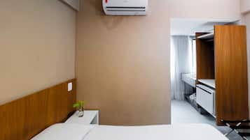 Een hotelkamer met een bed, een klein nachtkastje met een plant, een kledingkast en een airconditioning.