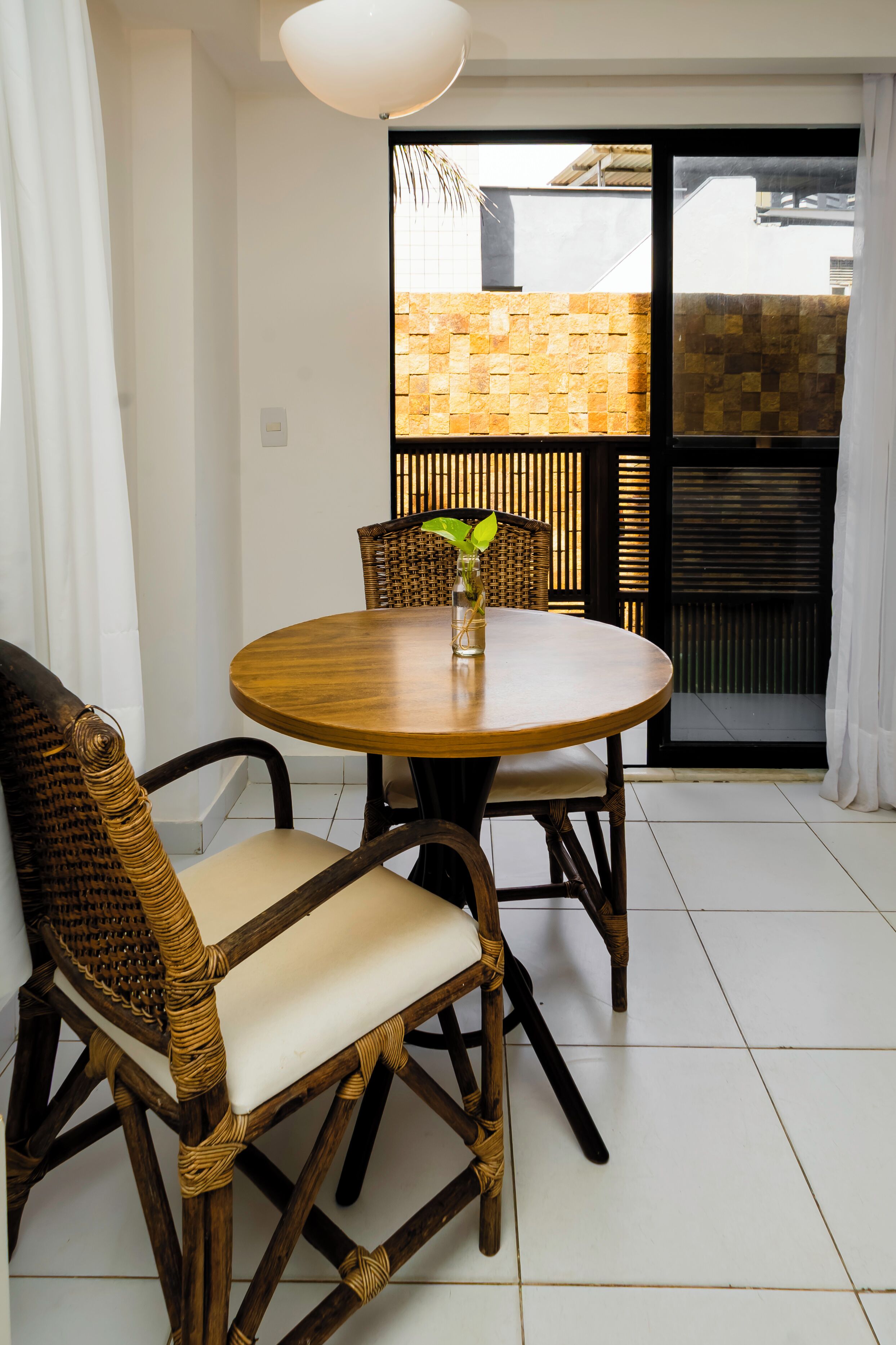 Comedor con una mesa redonda de madera, sillas de mimbre y un florero con una planta.