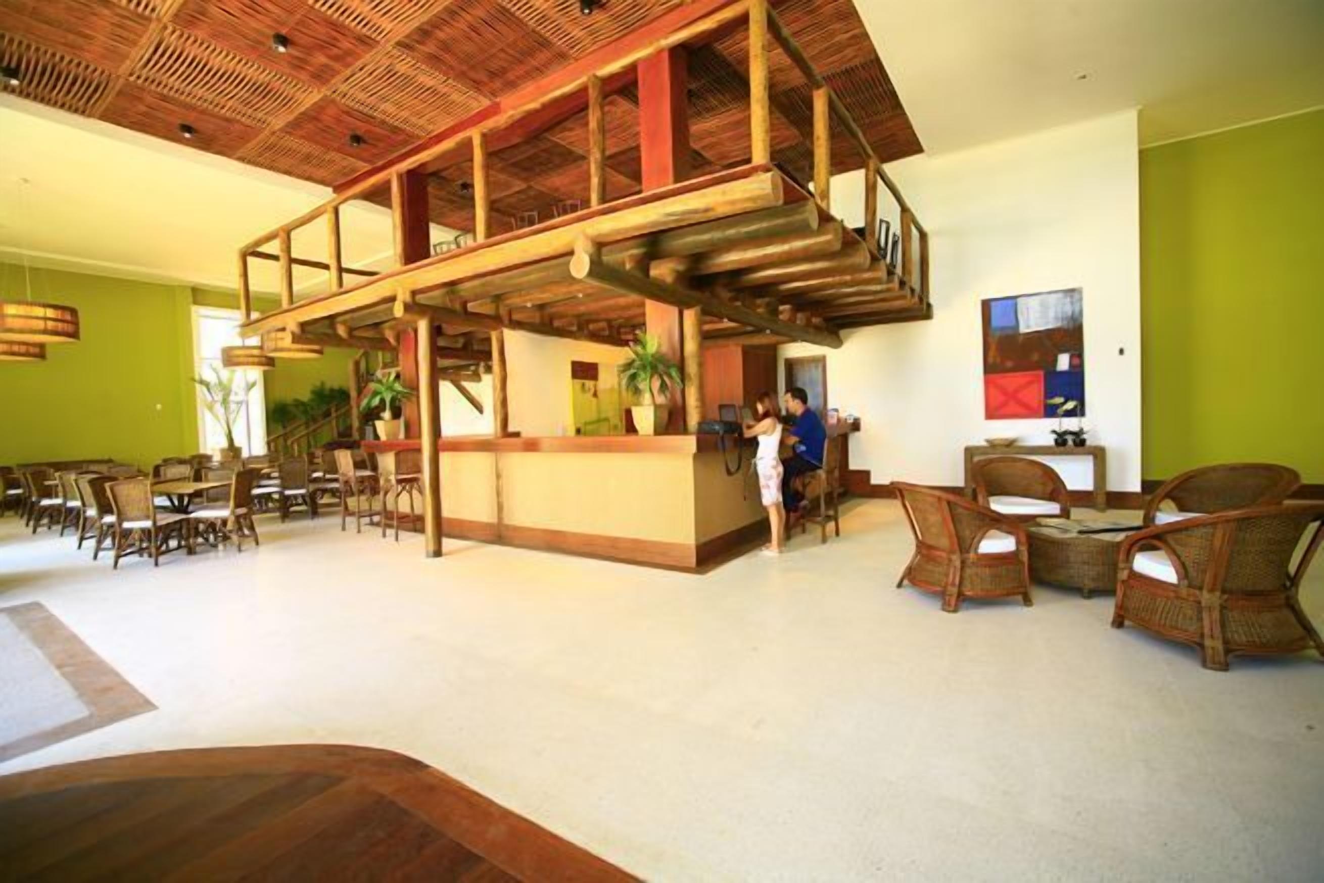 Un lobby espacioso con techo alto, una recepción, muebles de mimbre y una pared verde.