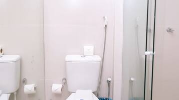 Un baño con inodoro, bidé y ducha con cerramiento de vidrio.