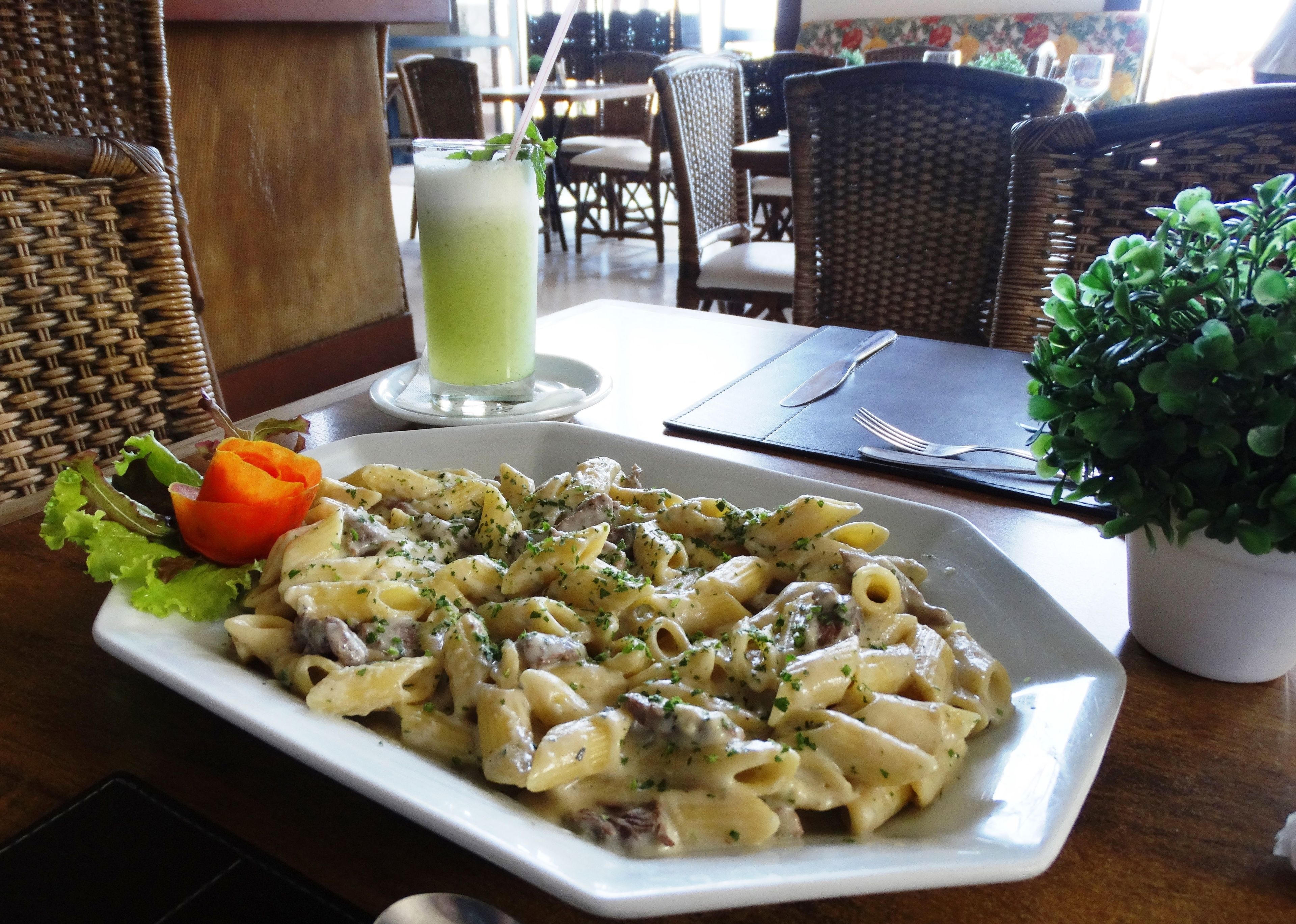 Ein Teller Pasta mit einem Salat und einem grünen Getränk auf einem Tisch in einem Restaurant.