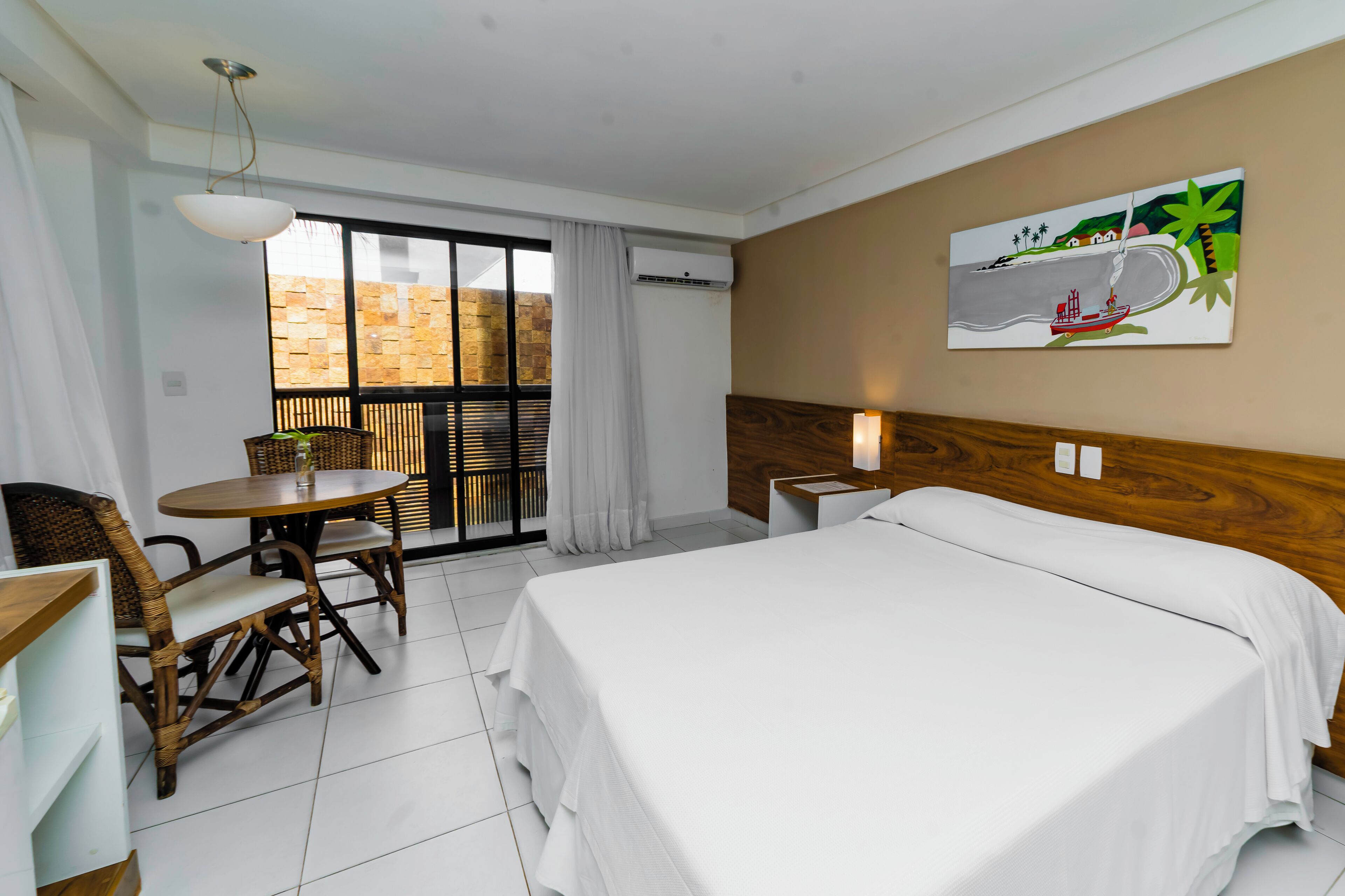 Una habitación de hotel con una cama, una mesa de comedor con sillas, un ventanal con vistas y un cuadro en la pared.