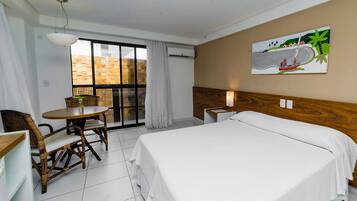 Una habitación de hotel con una cama, una mesa de comedor con sillas, un ventanal con vistas y un cuadro en la pared.