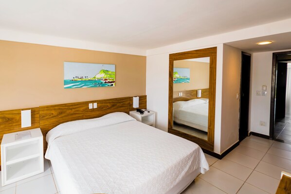 A hotel room with a large bed, a nightstand, a mirror, and a painting of a coastal scene.