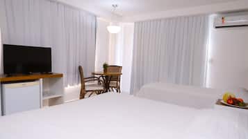 A hotel room with a bed, a TV, a small table with chairs, and a fruit basket on the bedside table.