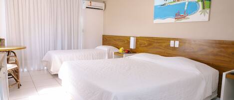 A hotel room with two beds, a wooden headboard, a painting of a beach scene, a small table with fruit, and a chair.