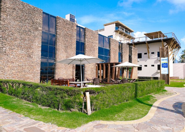 A hotel with stone exterior walls, outdoor seating with umbrellas, and a clear sky. - Porto Suites Natal Hotel (Natal)