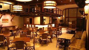 Un restaurante con mesas y sillas de madera, una barra y lámparas colgantes.