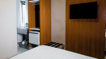 Habitación de hotel con cama, televisión montada en la pared, armario de madera y pequeña zona de kitchenette.