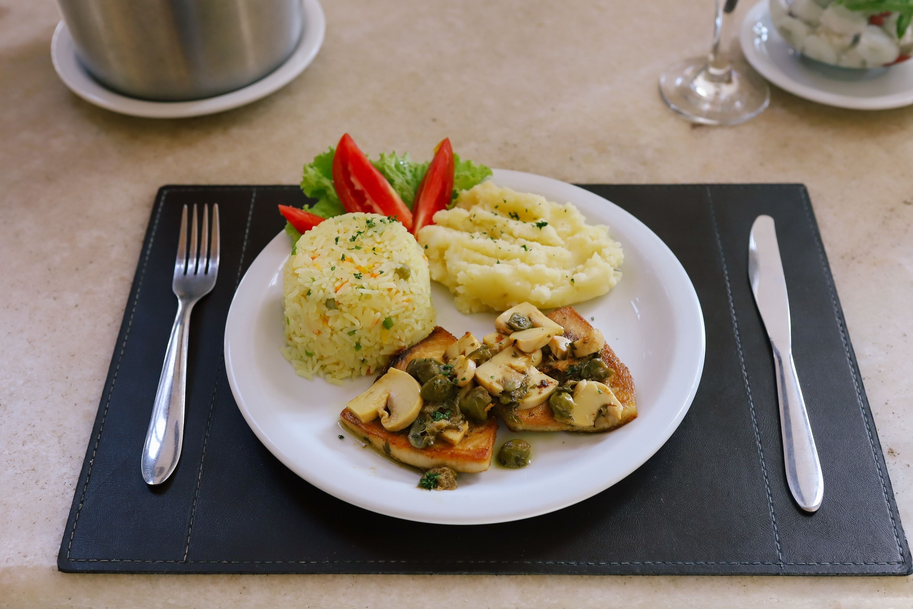 Une assiette de nourriture comprenant de la purée de pommes de terre, une salade verte et un plat de viande, le tout servi sur un set de table noir.